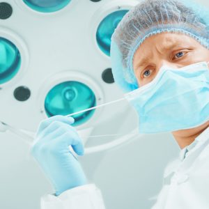 Young male surgeon doctor takes off his protective mask in operating room