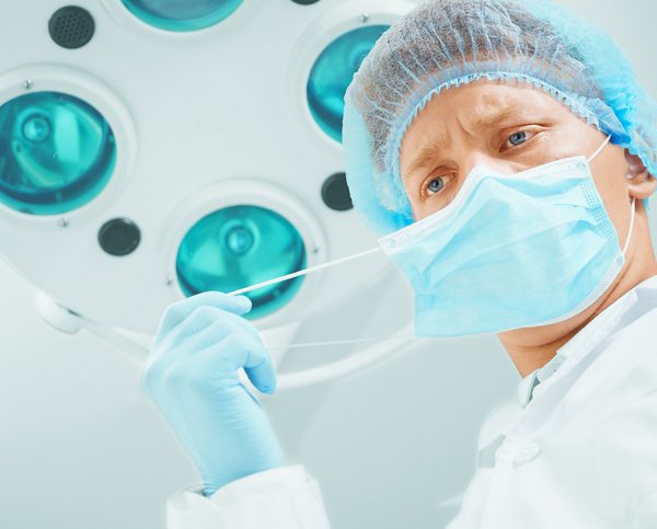 Young male surgeon doctor takes off his protective mask in operating room